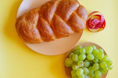 Şerit mezura ve sarı arka planda haşhaş tohumlu çörek. Sağlıklı gıda, diyet, kilo kaybı ve zayıflık kavramı. Tabakta üzümler