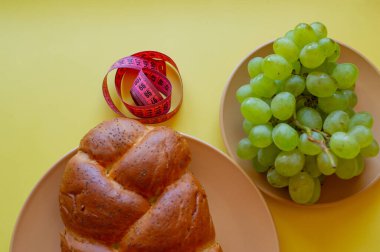 Şerit mezura ve sarı arka planda haşhaş tohumlu çörek. Sağlıklı gıda, diyet, kilo kaybı ve zayıflık kavramı. Tabakta üzümler