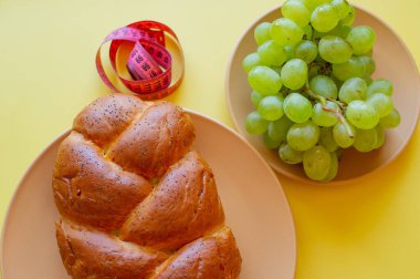 Şerit mezura ve sarı arka planda haşhaş tohumlu çörek. Sağlıklı gıda, diyet, kilo kaybı ve zayıflık kavramı. Tabakta üzümler