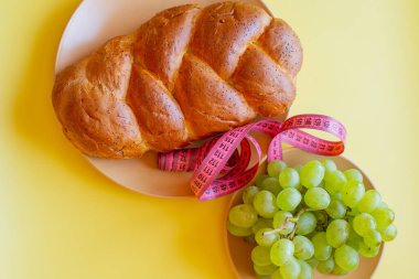 Şerit mezura ve sarı arka planda haşhaş tohumlu çörek. Sağlıklı gıda, diyet, kilo kaybı ve zayıflık kavramı. Tabakta üzümler