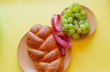 Şerit mezura ve sarı arka planda haşhaş tohumlu çörek. Sağlıklı gıda, diyet, kilo kaybı ve zayıflık kavramı. Tabakta üzümler