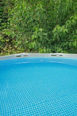 Bahçedeki bir ağacın arka planında su olan bir yüzme havuzu çerçevesi. Rahatlama