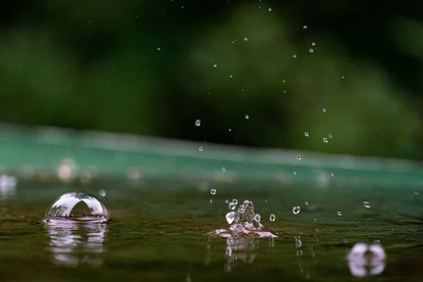 Close up of raindrops splattering on a green table — Stock Photo, Image