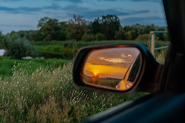 A golden sunset seen in an outside rear view mirror