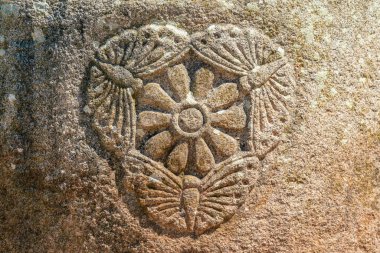 Eski taş bir çiçek duvarı ve üç kelebek oymak.