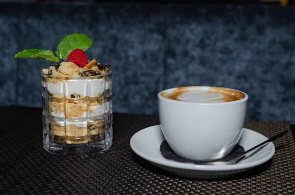 piece of honey cake in a glass and cup of cappuccino on dark table