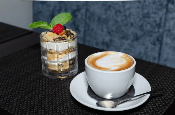 piece of honey cake in a glass and cup of cappuccino on dark table