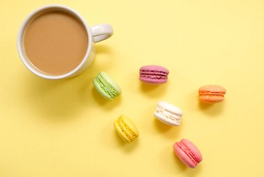 Renkli kurabiyeler ve kahve seti. Pastalar, hamur işleri ve sarı arka planda sütlü bir fincan kahve. Şekerleme. Günaydın. Uzayı kopyala Yukarıdan görünüm.