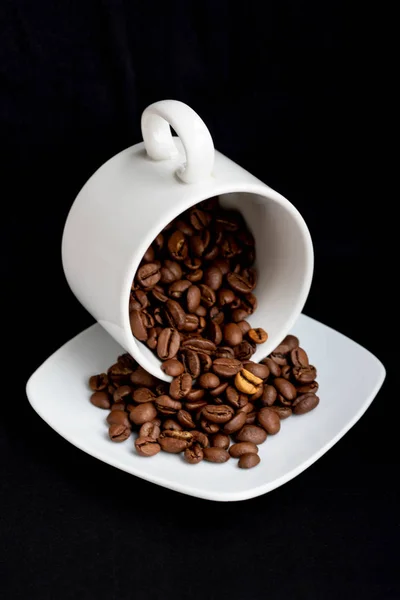 Una taza de café negro con granos de café tostados dispersos en la mesa negra sucia con manchas de café de fondo, vista superior . — Foto de Stock