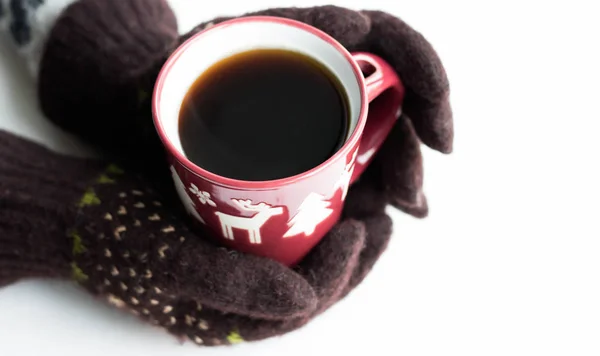 Χέρια σε καφέ γάντια με σχέδιο Πρωτοχρονιάς κρατήσει ένα κόκκινο κύπελλο με ζεστό καφέ σε λευκό φόντο. Top view Flat lay Χειμερινή κάρτα βράδυ — Φωτογραφία Αρχείου