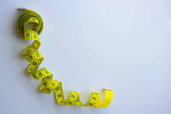 Tape measure in centimetrs as symbol of diet before summer time and healthy lifestyle, tailoring tool on white background.