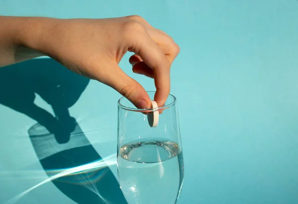 Niebieskim Tle Ręka Wrzuca Rozpuszczającą Się Tabletkę Aspiryną Szklanki Wody — Zdjęcie stockowe