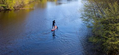 Bir adam bahar nehrinde bir kürek tahtasında yüzüyor. Onun yüzünü göremiyorum..