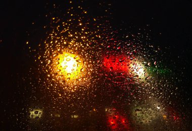Rain drops on window with road light bokeh,water drop on the glass, night storm raining car driving concept. night car