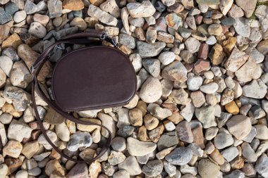 Bir kadının kahverengi çantası renkli taşların üzerinde yatıyor. Metnin için boşluk