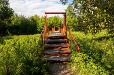 Küçük bir orman nehri üzerinde ahşap döşemeli ve demir kemerli küçük kırmızı bir köprü..
