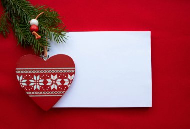 Kutlama kompozisyonu Notepad, beyaz süslemeli kırmızı ahşap kalp ve kırmızı arka planda yeşil köknar dalları. Noel ve Sevgililer Günü konsepti.
