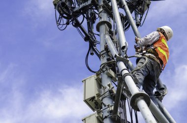 Telekomünikasyon kulesinde gökyüzü arka planına karşı çalışan teknisyen, yüksek riskli iş konsepti 