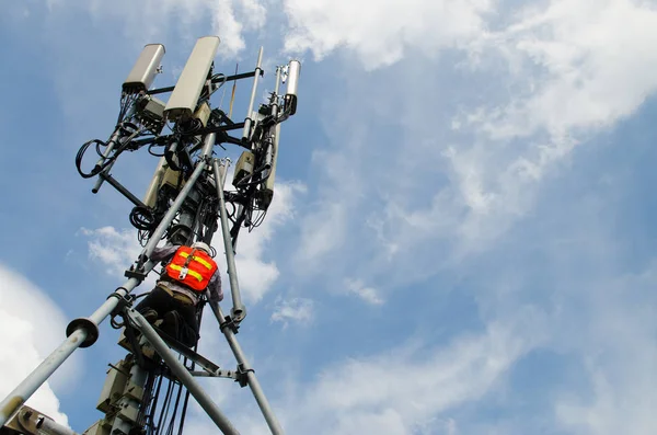 Technician working on telecommunication tower against sky background, high risk work concept