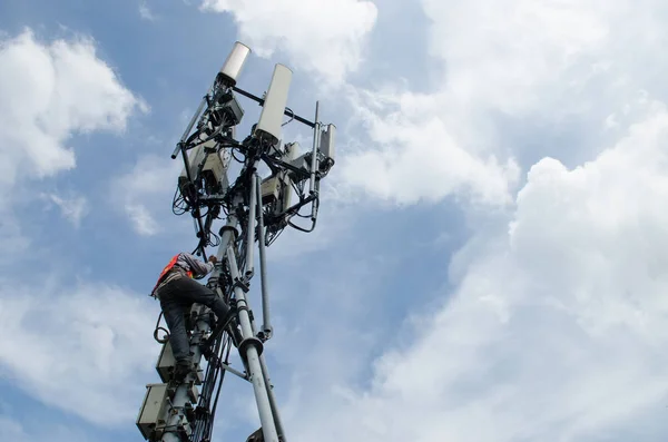 Technician working on telecommunication tower against sky background, high risk work concept