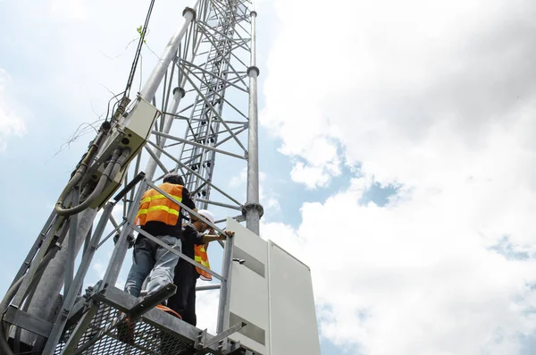 Technician working on telecommunication tower against sky background, high risk work concept