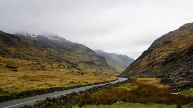 Kışın Snowdon'da yapılan bir yürüyüş sırasında yakalanan göl, engebeli vadi ve karamsar gökyüzünü n üstünden çarpıcı dağ manzarası (Snowdonia Ulusal Parkı, Galler, Birleşik Krallık)