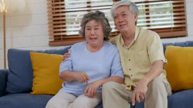 Gülümseyen asya üst düzey çift oturma odasında kanepede oturan ve evde Tv izlerken.