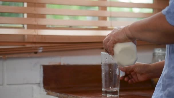 自宅の台所のガラスに注ぐミルクのボトルを保持しているクローズアップシニアアジアの女性 — ストック動画