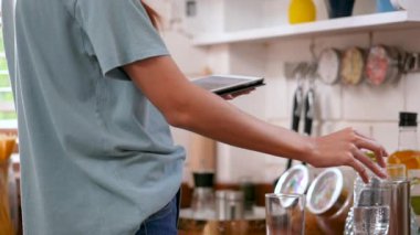 Mutlu genç asyalı kadın bir bardak su teslim ve tablet kullanarak. evde mutfakta teknoloji, sosyal ağ, iletişim konsepti.