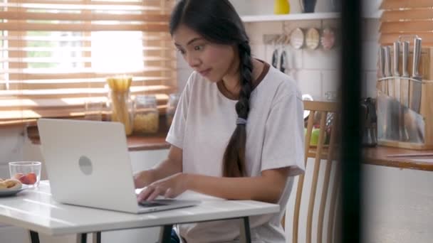 年轻的亚洲妇女快乐微笑使用笔记本电脑在家里的厨房 — 图库视频影像