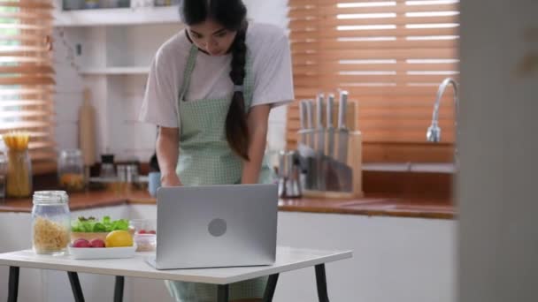 年轻的亚洲妇女使用笔记本电脑和原料做沙拉 草莓做饭一个健康的早餐在厨房在家里 — 图库视频影像