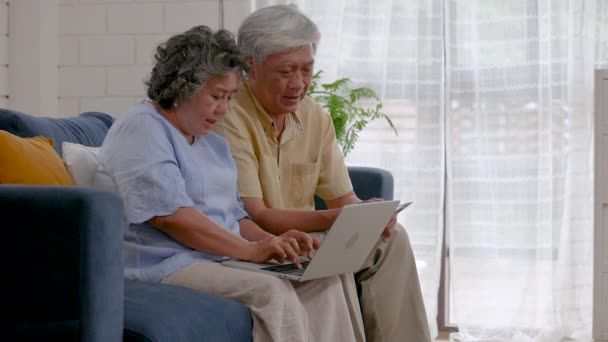 亚洲老年夫妇使用笔记本电脑搜索网上购物 在家中的客厅里分享社交媒体交流 慢动作 — 图库视频影像