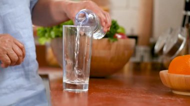 Yakın el kıdemli kadın evde mutfakta cama su dökerek.