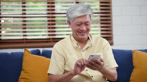 使用智能手机搜索网上购物的亚洲资深男子的肖像 分享社交媒体沟通坐在客厅的房间里的社交媒体上 — 图库视频影像