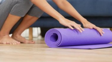 Genç asyalı kadın evde oturma odasında güvenli ve rahat yoga asanas gerçekleştirmek için yoga mat haddeleme.