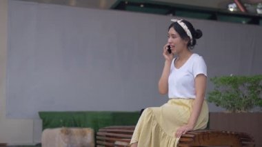 Portre genç Asyalı kadın otururken telefonda gülümseyerek ve mutluluk konuşuyor. Teknolojiyi kullanarak güzel genç iş yaşam tarzı.