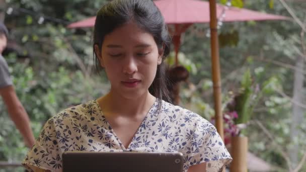 Fiatal ázsiai nő használ egy tablettát egy kávézóban. Technológiai szociális média.