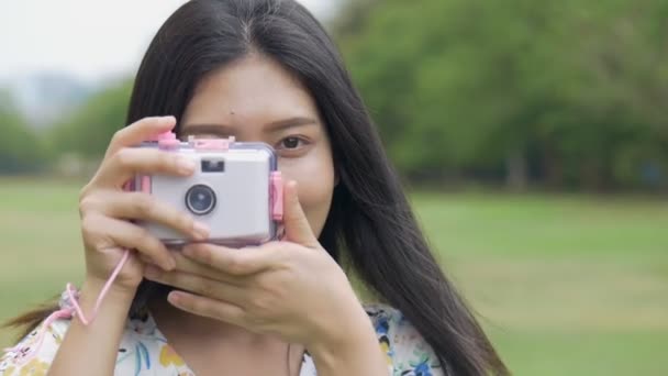 公共の公園で屋外でおもちゃのカメラで写真を撮って楽しむスローモーション美しいアジアの女性 — ストック動画