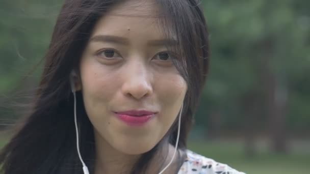 慢动作美丽的年轻亚洲女人喜欢听音乐看相机微笑在公共公园 — 图库视频影像