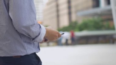 Asyalı işadamı yürüyüş ve akıllı telefon kullanarak kapatın. Gözlüklü Asyalı bir adam büyük bir ofis binasının yanındaki sokakta telefon kullanıyor..