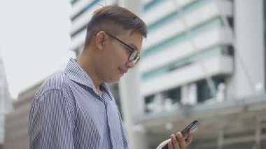 Yavaş çekim portre Asyalı işadamı telefon adabı yanıtlar. Gözlüklü Asyalı bir adam büyük bir ofis binasının yanındaki sokakta telefon kullanıyor..