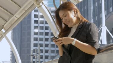 Gülümseyen genç Asyalı kadın şehir arka planda bir akıllı telefon bir arkadaşı ile mesajlaşma, sosyal medya arıyor.