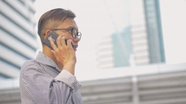 Yavaş çekim portre Asyalı işadamı telefon adabı yanıtlar. Gözlüklü Asyalı bir adam telefonu büyük bir ofis binasının yanındaki sokakta kullanıyor..