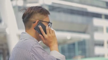 Yavaş çekim portre Asyalı işadamı telefon adabı yanıtlar. Gözlüklü Asyalı bir adam telefonu büyük bir ofis binasının yanındaki sokakta kullanıyor..