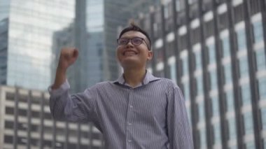 Portre yakışıklı Asyalı işadamı bir çalışma dan sonra başarı ve başarı bir kentsel şehir etrafında bakarak ayakta var. Yavaş çekim düşük açı çekimi.