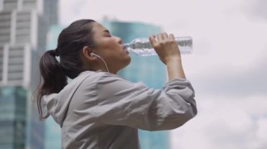 Portre genç Asyalı kadın koşucu çalışan ve halka açık bir parkta müzik dinledikten sonra su içmek.