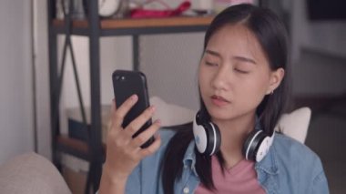 Güzel genç Asyalı kadın evde oturma odasında kanepede otururken akıllı telefon kullanarak görüntülü sohbet. Sosyal medya için kız selfie video fotoğraf. Yavaş çekim çekimi.