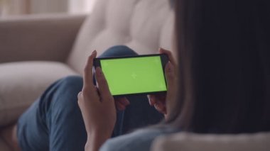 Çekici genç Asyalı kadın evde oturma odasında kanepede otururken sosyal medya tarama cep telefonu yeşil ekran görüntüleme. iş kadını akıllı telefonda video izlerken zevk. Yavaş çekim çekimi.