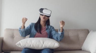Çekici portre genç Asyalı kadın oturma odasında vr kulaklık giyiyor, oyun oynarken, bir film izlerken. Sanal gerçeklik kulaklık takmak.