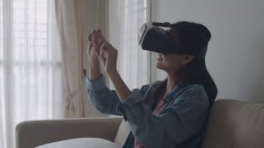 Çekici portre genç Asyalı kadın oturma odasında vr kulaklık giyiyor, oyun oynarken, bir film izlerken. Sanal gerçeklik kulaklık takmak.